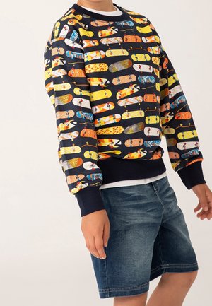 Sweat-shirt imprimé avec des motifs colorés de skateboard sur fond bleu marine. Poignets et ourlet côtelés. Associé à un short en denim.