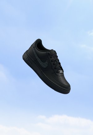 Baskets Nike Air Force 1 noires avec lacets et logo, flottant sur un fond de ciel bleu clair.