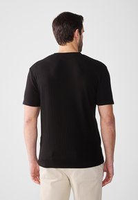 Sort ribbet t-shirt med korte ærmer, rund halsudskæring og slim fit. Bagfra vises tekstilens struktur og ren skrædderarbejde.