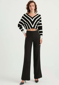 Svartvit randig kort tröja med V-ringning, i kombination med höga, vida svarta byxor och svarta klackar.