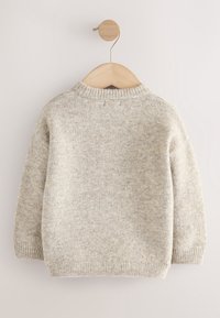 Pull en laine tricotée gris clair à manches longues suspendu à un cintre en bois sur fond blanc.