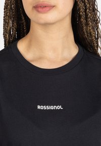 Camiseta de algodón negra con cuello redondo y un logo blanco "ROSSIGNOL" en la parte delantera. Textura suave y mangas cortas.