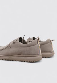 Scarpe in suede beige con una forma arrotondata, caratterizzate da una tomaia strutturata, lacci e un accento a righe sul tallone. Suola in gomma scanalata.