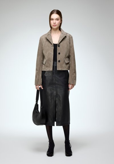 Brown suede cropped jacket with a pointed collar and three buttons, paired with a black leather midi skirt. Black heeled shoes and a shoulder bag.