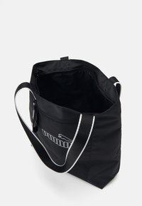 Sac fourre-tout en nylon noir avec des accents blancs, doté d'une fermeture éclair supérieure, d'une doublure intérieure et d'un logo à l'avant. Bandoulière réglable incluse.