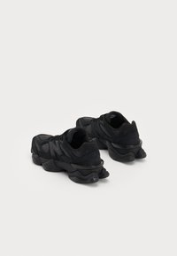 Baskets de sport noires avec un dessus texturé, une semelle courbée distinctive et une marque visible. Design élégant avec des matériaux contrastants.