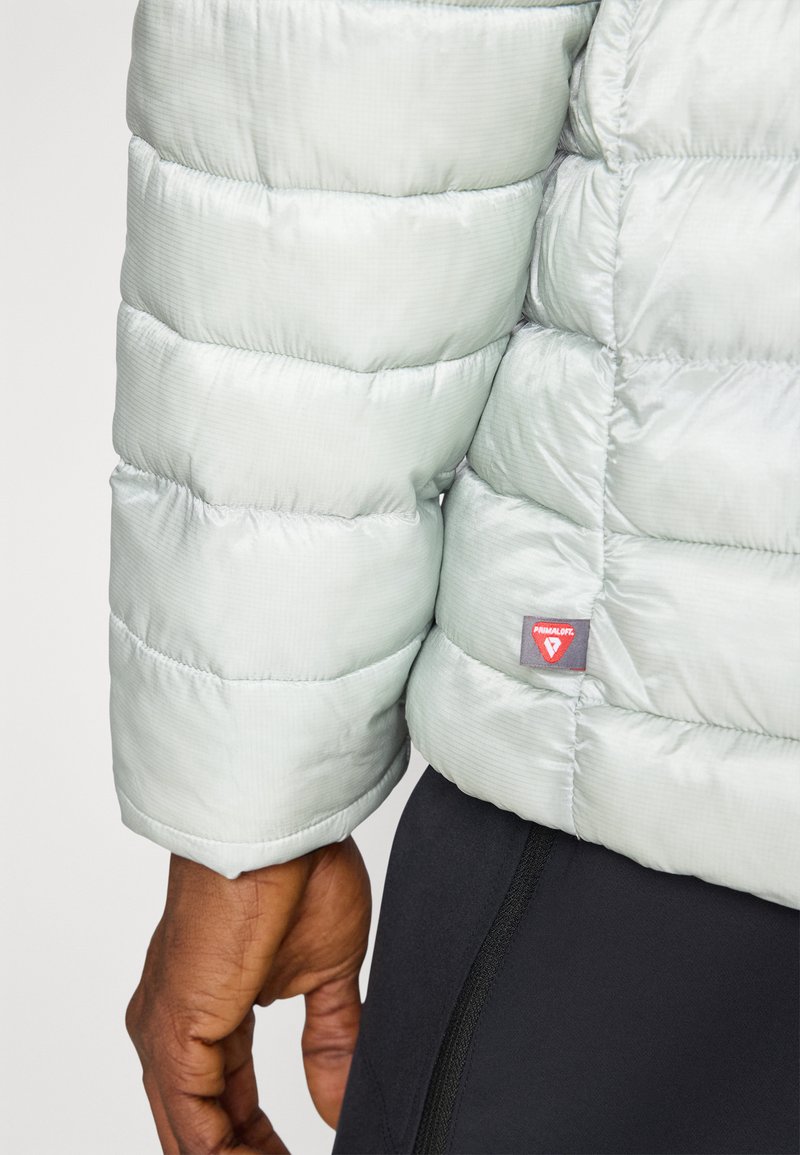 Jasnozielona kurtka puchowa z pikowanymi sekcjami, posiadająca gładką powierzchnię i metkę Primaloft. Uzupełniona eleganckim wzorem mankietów.