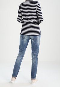 Marineblau-weiß gestreiftes Langarmshirt trifft auf hellblaue Slim-Fit-Jeans mit ausgewaschenen Details und weißen Sneakern, von hinten betrachtet.