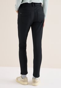 Zwarte slim-fit broek van zachte stof, met twee achterzakken en subtiele stiksels. Gecombineerd met lichtgekleurde sneakers.