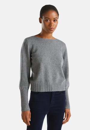Pull gris en tricot avec un ourlet et des poignets côtelés, dotés d'un col rond et d'une coupe décontractée. Associé à un pantalon en velours côtelé bleu foncé.