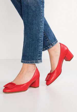 Røde læder sko med blokhæle, rund tå og en stor firkantet spænde detaljer på forsiden, parret med opsmøgede blå jeans.