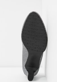 Semelle de chaussure à talon haut à bout pointu avec tige à motif, semelle en caoutchouc noir embossée du mot "Tamaris" en répétition.