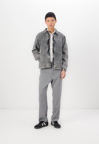 Denim jacket in faded gray with a button-up front, worn over a white and black checkered shirt, paired with gray trousers and black sneakers.