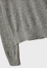 Dettagli delle maniche e dell'orlo di un morbido maglione grigio a maglia su sfondo bianco, che mostrano la texture e le finiture a coste.