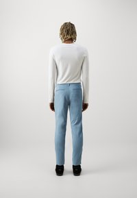 Jasnoniebieskie spodnie o slim fit z tylnymi kieszeniami. W zestawieniu z białą koszulą z długim rękawem. Materiał wydaje się gładki i casualowy.
