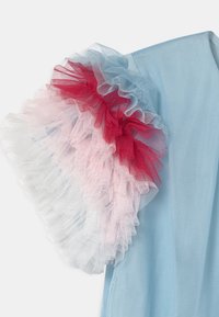 Vêtement bleu clair avec une manche à volants. La manche est superposée de tulle rouge, rose et blanc, créant une texture et un contraste de couleurs.