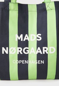 Borsa a spalla a righe verdi e blu con il testo "MADS NØRGAARD COPENHAGEN" in lettere bianche in grassetto. Realizzata in tessuto resistente.