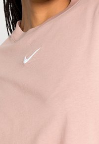 Ljust rosa bomullströja med rundad halsringning och en liten vit Nike-logga broderad på bröstet. Slät textur.