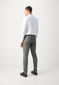 Men's outfit featuring a white long-sleeve shirt and olive green slim-fit pants, with black loafers and a smooth texture.