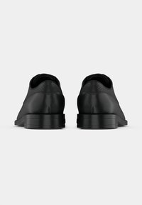 Scarpe formali nere in pelle con dettaglio testurizzato sul tacco, viste da dietro su uno sfondo chiaro e uniforme.