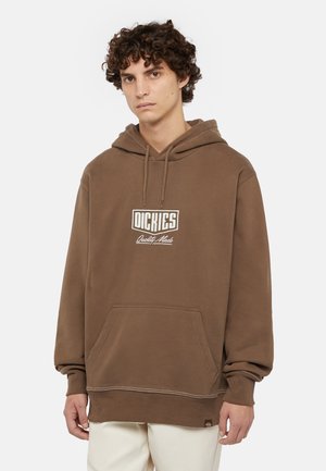Bruine hoodie van zacht materiaal met een voorzak, voorzien van een wit logo en stikdetails aan de onderkant en mouwen.