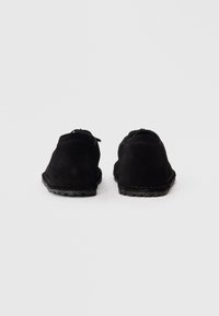 Ein Paar schwarze Wildlederschuhe mit Gummisohlen, von hinten auf einem weißen Hintergrund gezeigt.