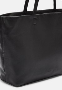 Zwarte leren tote bag met twee handvatten. Gladde textuur, gestructureerde vorm, subtiele branding aan de onderkant en geen aanvullende versieringen.