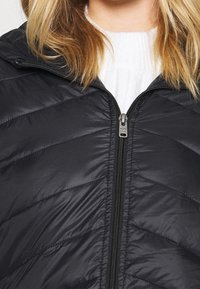 Veste matelassée noire avec une fermeture éclair frontale, un motif en chevrons et une capuche. Le matériau semble brillant et texturé, offrant une meilleure isolation thermique.