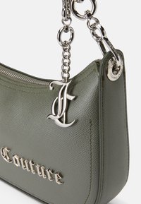 Zeleni kožni ručni torbica s teksturom koja ima srebrnu munjevitu zatvarač, metalne detalje i utisnuti natpis "Couture" na površini.