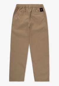 Beige katoenen broek met een elastische tailleband, taps toelopende vorm en een achterzak met een merklabel. Gladde textuur, geen patronen.