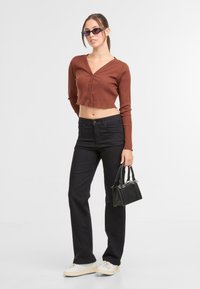 Skraćeni rebrasti smeđi kardigan, crne traperice visoko strukirane, bijele tenisice i mala crna torbica sa srebrnim detaljima.