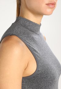 Top grigio senza maniche con colletto a imbuto dal design aderente, caratterizzato da una texture liscia e un lieve motivo melangiato sul tessuto.
