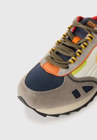 Sneaker met een grijze suède bovenkant, marineblauwe stof, oranje accenten en gele veters. Bevat een stevige zool met een gestructureerde zwarte loopvlak.