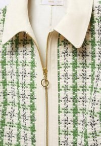 Giacca con colletto in tessuto crema, caratterizzata da righe verticali con motivi intrecciati verdi e neri. Include una zip dorata con un cursore circolare.