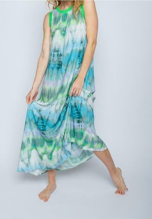 Femme pieds nus portant une robe sans manches fluide tie-dye en bleu, vert et blanc, soulevant l'ourlet en se tenant sur une jambe.