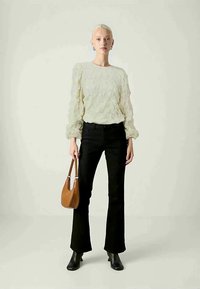Blusa testurizzata bianca sporca con maniche lunghe, abbinata a jeans neri a zampa d'elefante. Una borsa a spalla marrone e stivali neri alla caviglia completano l'outfit.