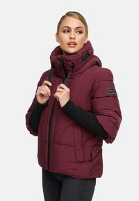 Burgunderfarbene Daunenjacke mit hohem Kragen, schwarzen Bündchen, Reißverschluss und Logopatch am Ärmel. Die gesteppten Strukturen bieten Wärme.