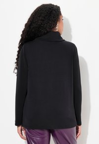 Top negro de manga larga con cuello de capa, textura suave y corte relajado. Se combina con pantalones morados brillantes.