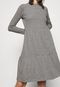 Abito grigio a maniche lunghe in un tessuto strutturato, con un corpetto aderente e una gonna a strati svasata. Collo rotondo semplice, design casual.