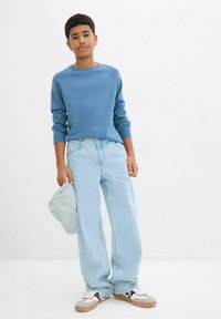 Maglione a maniche lunghe azzurro chiaro, jeans di denim leggeri e un berretto azzurro chiaro. Le sneaker presentano una combinazione di bianco, nero e beige. Vestibilità casual.