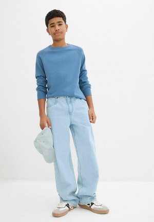 Pull à manches longues bleu clair, jeans en denim clair et casquette bleu clair. Les baskets sont un mélange de blanc, noir et beige. Style décontracté.