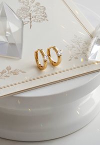 Guldhoopörhängen har en elegant design med en slät yta, prydda med en klar ädelstensdetalj på varje örhänge.