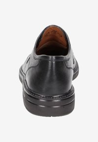 Zapato de piel negra con textura suave, tacón redondo y detalle de costura. El interior es de piel marrón, con una plantilla acolchada.
