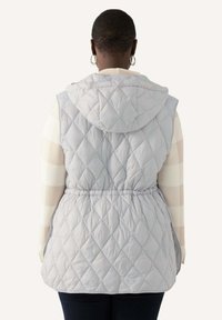 Ljust grå quiltad väst med huva, elastisk midja och diamantmönster. Baksidan har en slät yta och en avslappnad, lös passform.