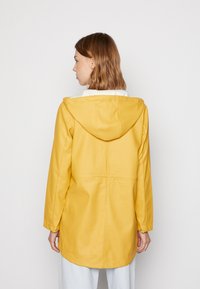 Geacă galbenă impermeabilă cu glugă, având o croială lejeră, mâneci lungi și o textură mată, fină. Fără elemente de prindere sau modele vizibile.