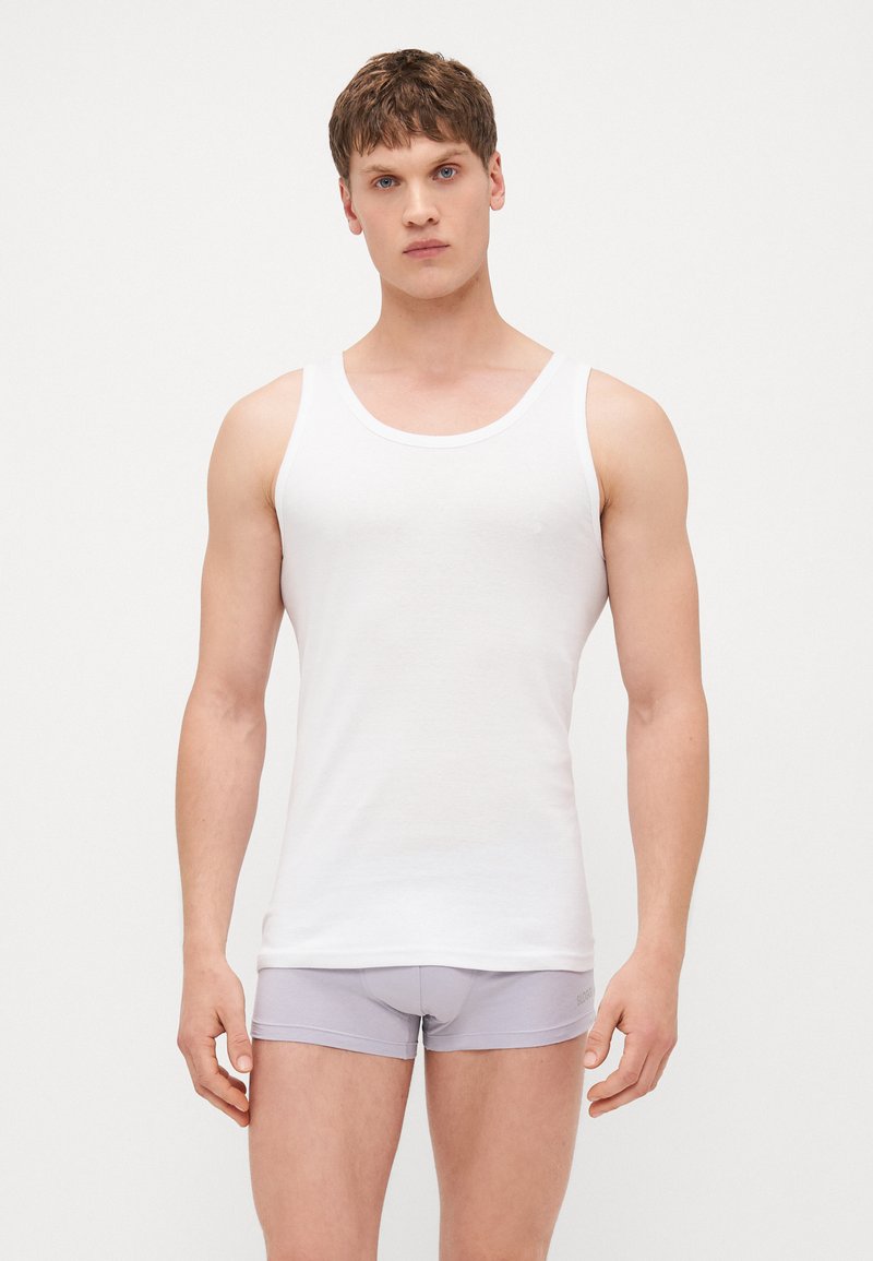 Bijela bezrukavna majica od mekog pamučnog materijala, sa zaobljenim izrezom i ravnim donjim rubom. Nosi se uz svijetlosive bokserice.