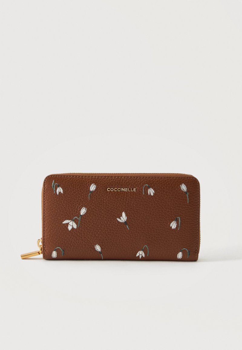 Portefeuille en cuir marron avec fermeture éclair tout autour, petite broderie fleur blanche et logo doré "COCCINELLE" sur le devant.