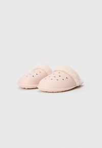 Une paire de pantoufles légères roses claires à enfiler, avec des trous de ventilation et une doublure blanche duveteuse, inclinées légèrement vers la droite sur un fond uni.