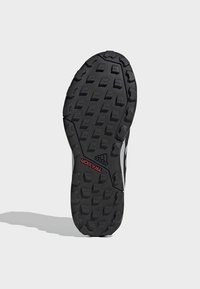 Semelle de chaussure Adidas noire avec des crampons profonds multidirectionnels, texte "TRAXION" rouge et logo Adidas proche du centre sur fond clair.