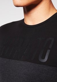 Černé tričko s krátkým rukávem, které má texturovaný, vystouplý design se slovem "MORATO" velkými písmeny přes hruď, hladký materiál.